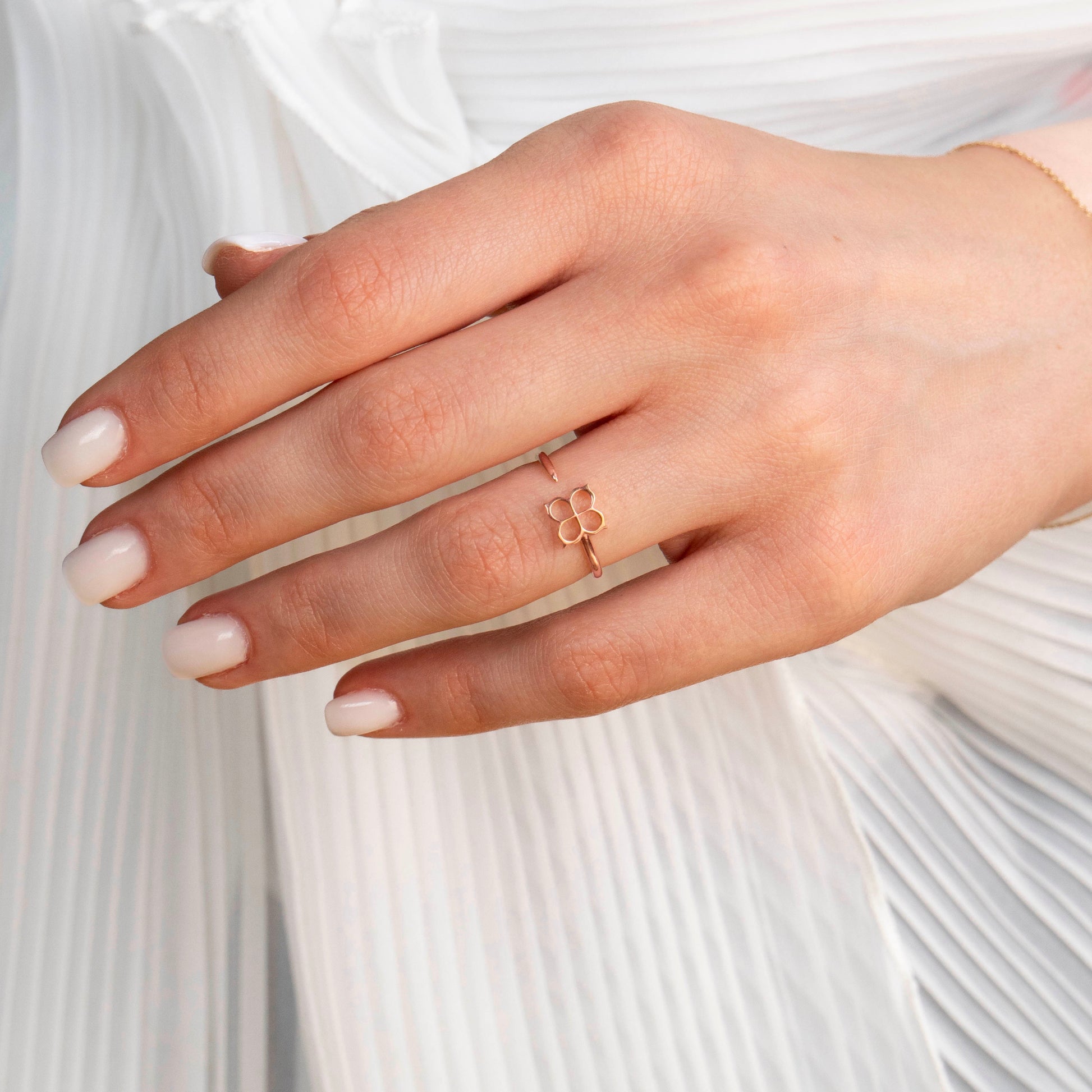Hand wearing a delicate rose gold ring with a floral design against a white background